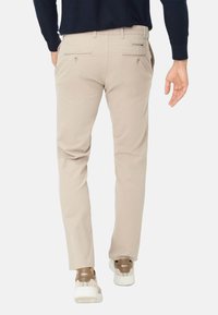 Beige chino's van katoen met een slim fit, voorzien van ritszakken aan de achterkant en een platte voorkant. Gecombineerd met lichte sneakers.