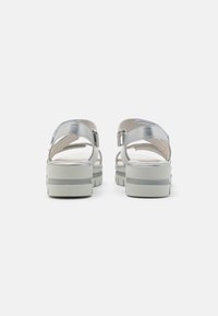 Sandali platform in argento con cinturini incrociati, una cinturino alla caviglia regolabile e suola bianca testurizzata. Luminosità metallica evidente sul materiale superiore.