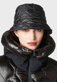 Giubbotto a vento trapuntato nero con colletto alto e chiusura con zip, abbinato a un cappello a secchiello nero coordinato con un motivo testurizzato.