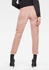 Osoba ve zkrácených růžových kalhotách a černých vysokých ponožkových botách na podpatku, stojící s jednou rukou opřenou o bok.