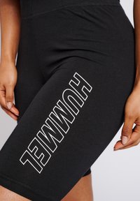 Zwarte katoenen fietsshorts met een verticale witte logo aan de zijkant. Glad textuur met een aansluitend ontwerp en een lengte tot halverwege de dij.