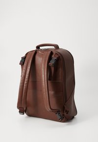 Sac à dos en cuir marron avec des bretelles réglables, une poignée supérieure et une texture lisse. Il dispose d'une fermeture éclair et de accents en matériel robuste.