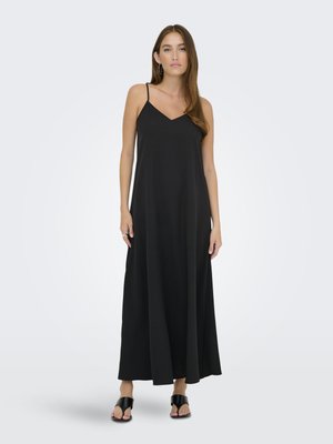 Robe maxi noire avec des fines bretelles, décolleté en V profond, silhouette fluide et tissu lisse. Portée avec des sandales glissantes noires.