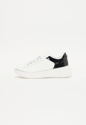 Baskets blanches avec talon noir, lacets blancs et semelle épaisse blanche, présentées de profil sur un fond blanc uni.