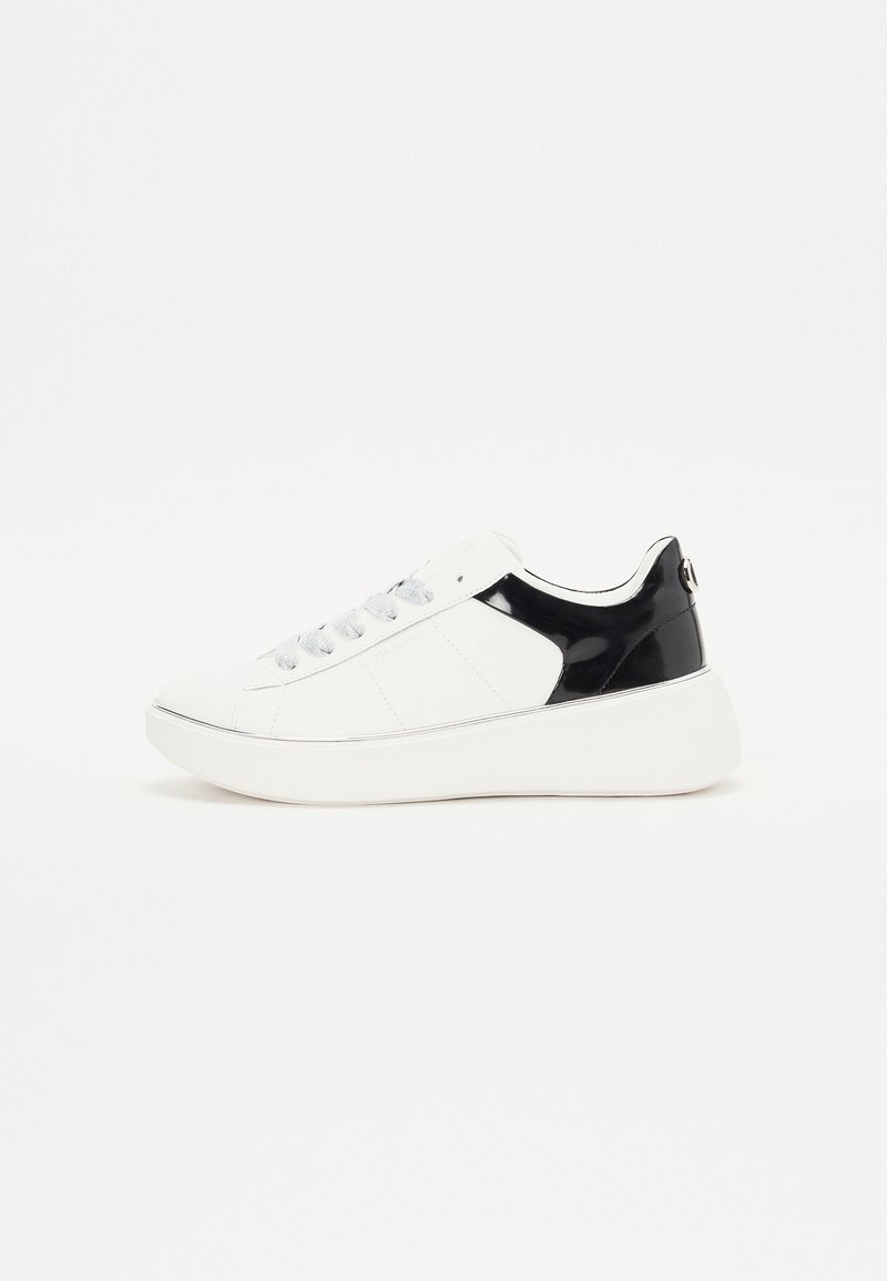 Baskets blanches avec talon noir, lacets blancs et semelle épaisse blanche, présentées de profil sur un fond blanc uni.