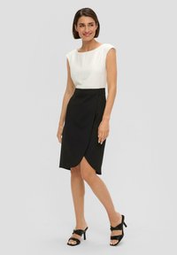Robe noir et blanc avec un corsage ajusté et une jupe enveloppante. Tissu lisse, manches courtes et ourlet au genou. Associée à des sandales à talons noirs.
