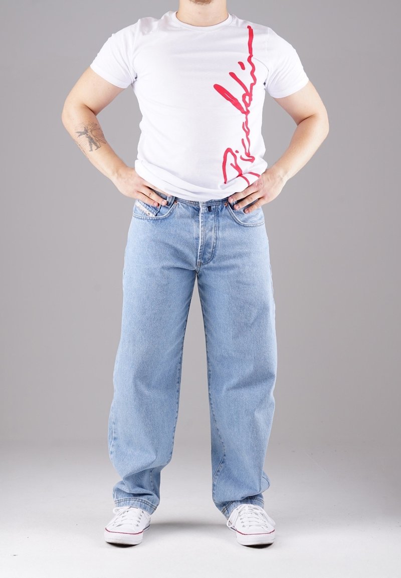 Valkoinen t-paita, jossa punainen painatus sivussa, yhdistetty vaaleansinisiin leveälahkeisiin farkkuihin ja valkoisiin tennareihin. Yksinkertainen malli ja rento istuvuus.