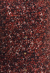 Tessuto della camicia con stampa animale rossa e nera con superficie tessurizzata, presenta bottoni dorati lungo la parte frontale e un design con colletto.