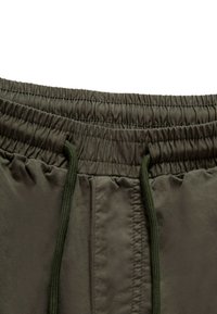 Fascia elastica verde scuro con cordoncino regolabile; tessuto liscio e strutturato; tasche laterali visibili.