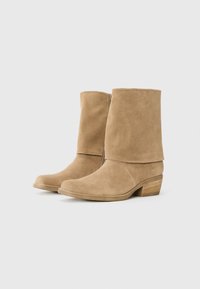 Bottines en daim taupe avec un dessus légèrement plié, un bout arrondi et un petit talon empilé. Détail de fermeture éclair sur le côté pour un enfilage facile.