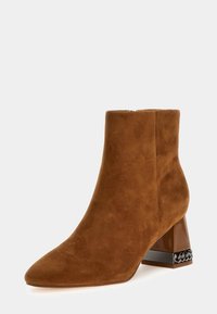 Stivale alla caviglia in suede marrone con punta affusolata e tacco a blocco trasparente caratterizzato da dettagli intrecciati neri. Texture liscia in tutta la superficie.