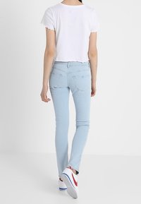 Vaqueros ajustados de un azul claro con cintura alta, dobladillo deshilachado y bolsillos traseros, combinados con una camiseta blanca corta y zapatillas deportivas.
