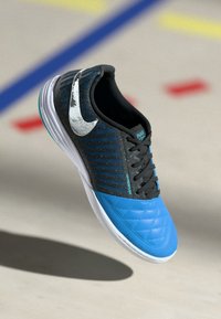 Juodas ir mėlynas sportinis batas su margintu priekiu, dryžuota viršumi ir sidabriniu Nike swoosh logotipu. Guminis padas ir raištelių užsegimas.