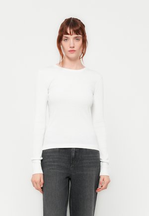 Hvit langermet skjorte med rund hals og ribbestruktur, kombinert med mørkegrå bukser. Enkelt og minimalistisk design.