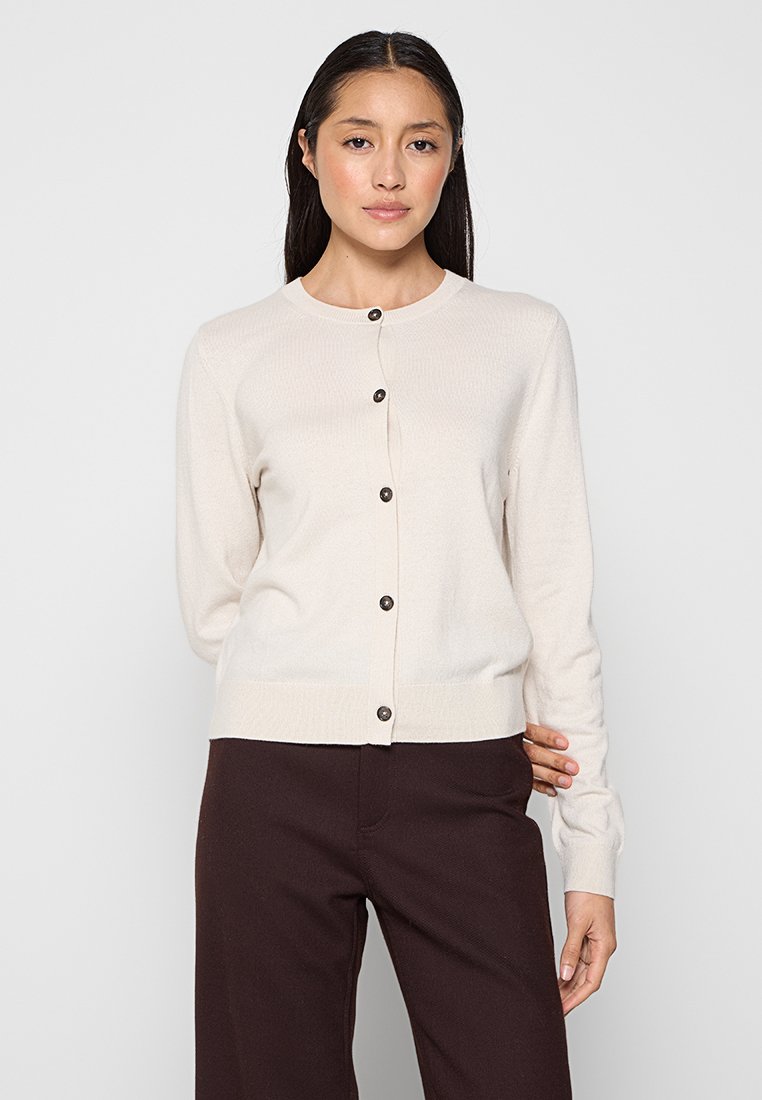 Helles beige Strickjacke aus weichem Material, mit rundem Hals, langen Ärmeln und braunen Knöpfen auf der Vorderseite.
