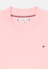 Roosa kudumisega kampsun ribbelise kaelusega, mille vasakul küljel on väike tikandlogoga. Kanga tekstuur näeb välja pehme ja peen.