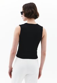 Top negro sin mangas en tejido acanalado con un diseño ajustado y escote redondo, combinado con pantalones blancos de cintura alta.