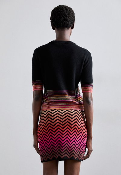 Vestido de malha com um topo preto e vibrantes detalhes listrados, transicionando para um padrão em ziguezague em tons graduais de rosa e laranja.