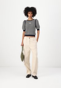 Maglione a righe in navy e bianco con maniche a palloncino corte, abbinato a pantaloni beige a vita alta e gamba ampia, e una borsa verde.