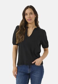 Black short-sleeved blouse with a V-neck and gathered puff sleeves. Smooth fabric with a relaxed fit. Worn with blue denim jeans.