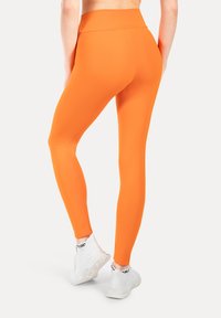 Hoge taille, strakke leggings in feloranje, gemaakt van rekbaar materiaal, gecombineerd met witte sportschoenen. Zachte textuur zonder zichtbare patronen.