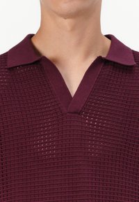 Pull en maille bordeaux avec un col, doté d'une texture en grille et de manches courtes. Le tissu est léger et respirant.