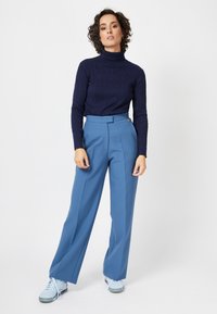 Pull à col roulé côtelé marine associé à un pantalon large taille haute bleu clair et des baskets bleu clair. Design simple, texture douce.