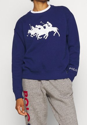 Navy sweatshirt with white polo players on horses graphic, paired with gray sweatpants featuring red and navy "POLO" text on thigh.