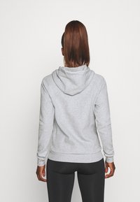 Hoodie gris en tissu doux, doté d'une poche kangourou et d'une capuche à cordon. Fini avec des poignets et un ourlet côtelés.