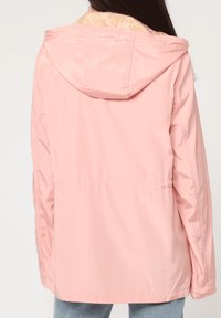 Chaqueta de lluvia rosa claro con capucha, con un forro texturizado y con patrón. Diseño sencillo, longitud media y un corte relajado con bolsillos laterales.