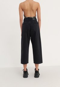 Černé džíny s vysokým pasem a širokými nohavicemi, zkrácené délky, doplněné páskem a dvěma zadními kapsami. Kombinováno s černými teniskami.