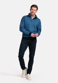 Blauwe pullover sweatshirt met kraag en gedeeltelijke rits, gecombineerd met donkere broeken en crèmekleurige sneakers. Zacht materiaal en een aansluitend ontwerp.