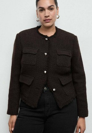 Giacca marrone con trama, quattro tasche frontali, orlo sfrangiato e collo rotondo. Presenta bottoni lucidi d'argento per la chiusura. Indossata su jeans neri.