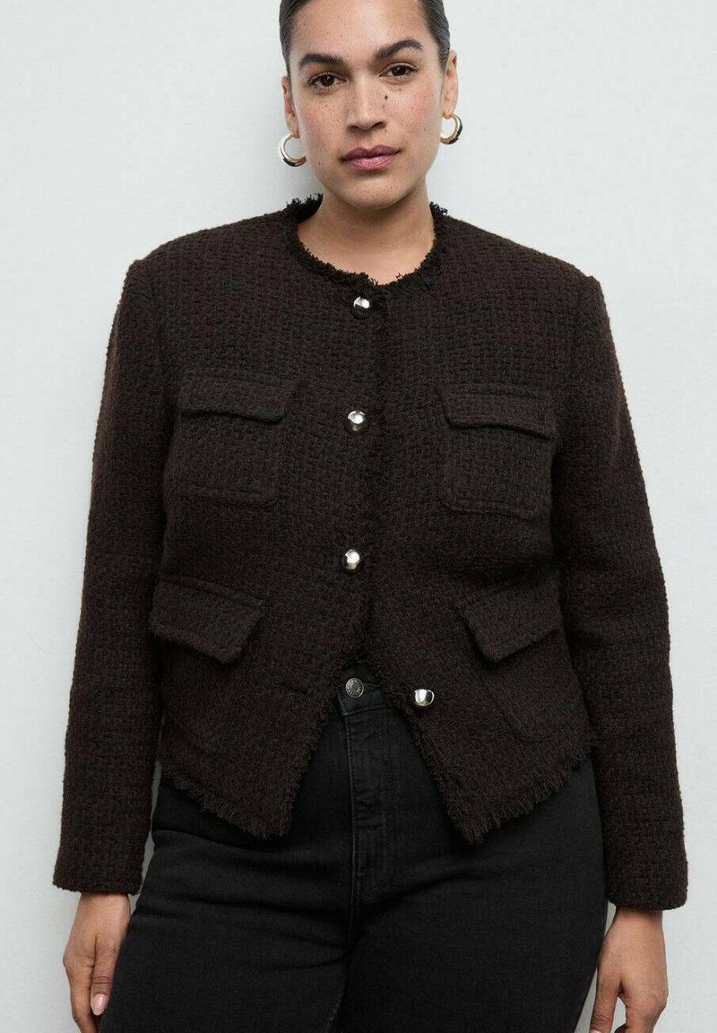 Veste marron texturée avec quatre poches avant, ourlet à franges et col rond. Dotée de boutons argentés brillants pour la fermeture. Portée sur un jean noir.