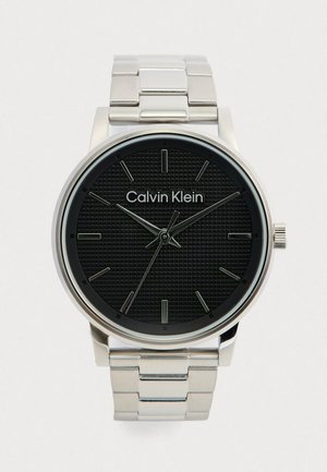 Calvin Klein óra fekete struktúrált számlappal, ezüstszínű rozsdamentes acél tok és karkötő, valamint visszafogott fémszínű órabeosztókkal.