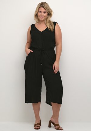 Svart ärmlös jumpsuit med V-ringning, elastisk midja, sidofickor och cropped vida ben. Bärs med bruna blockklacksandaler.