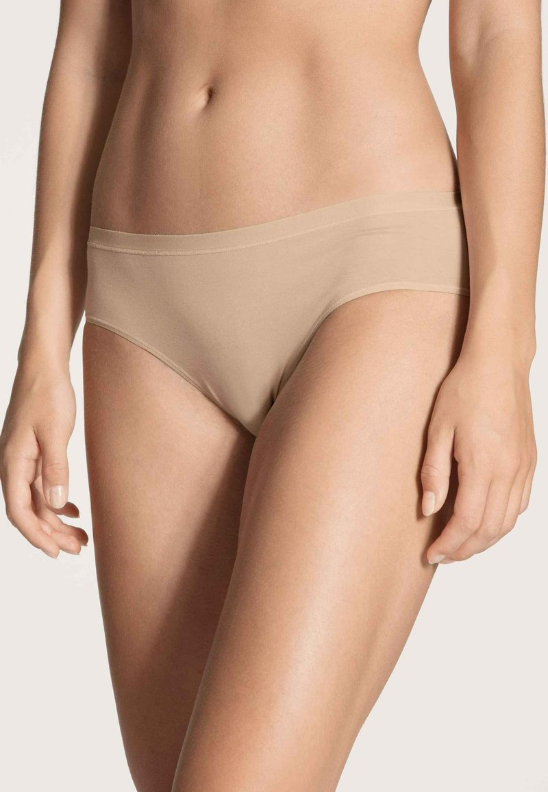 Beige naadloze ondergoed met een lage taille, een gladde textuur en een dunne elastische tailleband die de heupen omhelst zonder zichtbare lijnen.