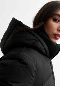 Czarna ocieplana kurtka z wysokim kołnierzem i dużym kapturem, o gładkiej fakturze i subtelnych detalach szycia wzdłuż szwów.