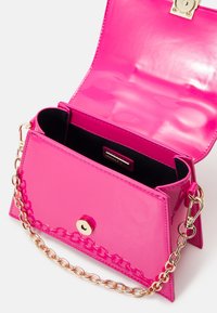 Sac à épaule en cuir verni rose vif avec bandoulière chaîne dorée, rabat ouvert et doublure intérieure noire.