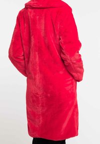 Cappotto in faux fur rosso con ampio colletto, maniche lunghe e taglio a lunghezza ginocchio. Tessuto liscio con una sottile lucentezza; senza chiusure visibili.
