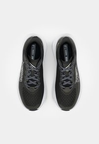 Baskets de sport noires avec des accents gris, dessus en maille, languette rembourrée et semelle extérieure blanche. Caractéristiques comprennent un système de laçage et un détail de logo.