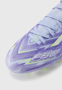 Purple and white soccer cleat with zigzag patterns, featuring green accents and a textured upper. Laces and logo visible on the side.