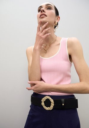 Top de tirantes rosa con canalé y ribete blanco, combinado con una falda azul oscuro con diseño texturizado. Cinturón negro adornado con una hebilla circular dorada y texturizada.