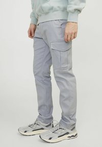 Hellgraue Cargo-Hosen mit Seitentaschen, schlankem Schnitt und robuster Stoffqualität, kombiniert mit grauen Sneakers, die über Mesh- und Texturfunktionen verfügen.