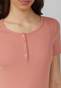 Jasnoróżowa ribbed T-shirt z okrągłym dekoltem, krótkimi rękawami i listwą z pięcioma dopasowanymi guzikami z przodu.