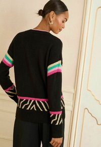 Melnā adīta džempera piedurkņās ir rozā, tirkīza un krēmkrāsas svītras, bet apakšmalā ir zebra raksta akcents. Ar teksturētu apdari.
