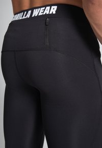 Black athletic leggings with a wide waistband featuring "Gorilla Wear" in white. Includes a small zip pocket at the back and flatlock seams.