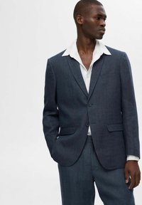 Giacca da suit blu navy su misura con revers a punta, chiusura con un bottone e due tasche laterali, indossata su una camicia bianca.