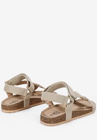 Sandali beige con suola in sughero, fasce in tessuto morbido, chiusure regolabili e design piatto con punta aperta.