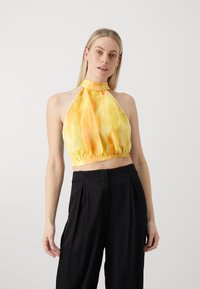Gelbes Halfter-Crop-Top mit einem strukturierten, gerafften Saum. Verfügt über einen hohen Kragen und fließenden Stoff; kombiniert mit schwarzen hoch taillierten Hosen.